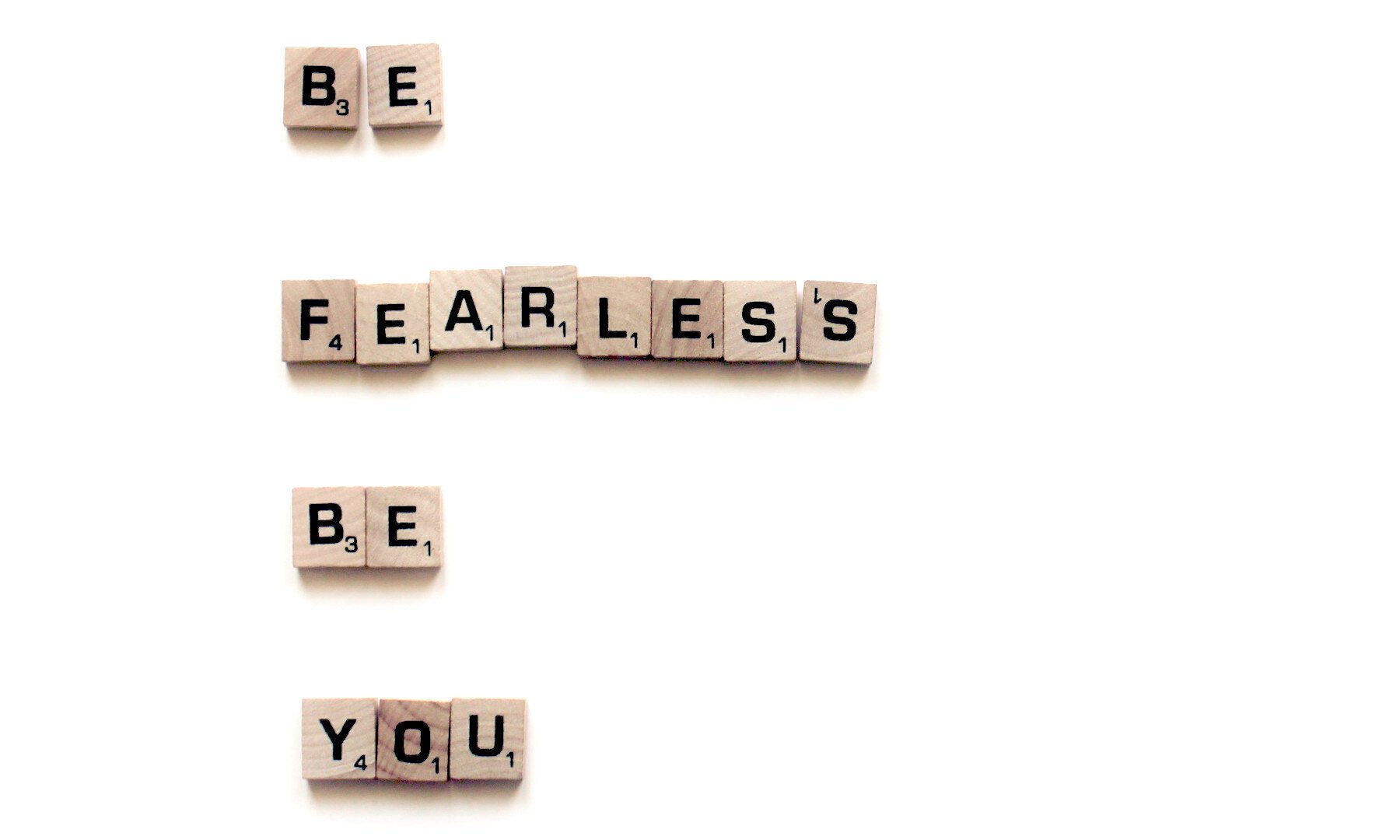Auf weißem Hintergrund sind die Wörter "BE FEARLESS BE YOU" gelegt. Es handelt sich um Holz-Scrabble Spielsteine.