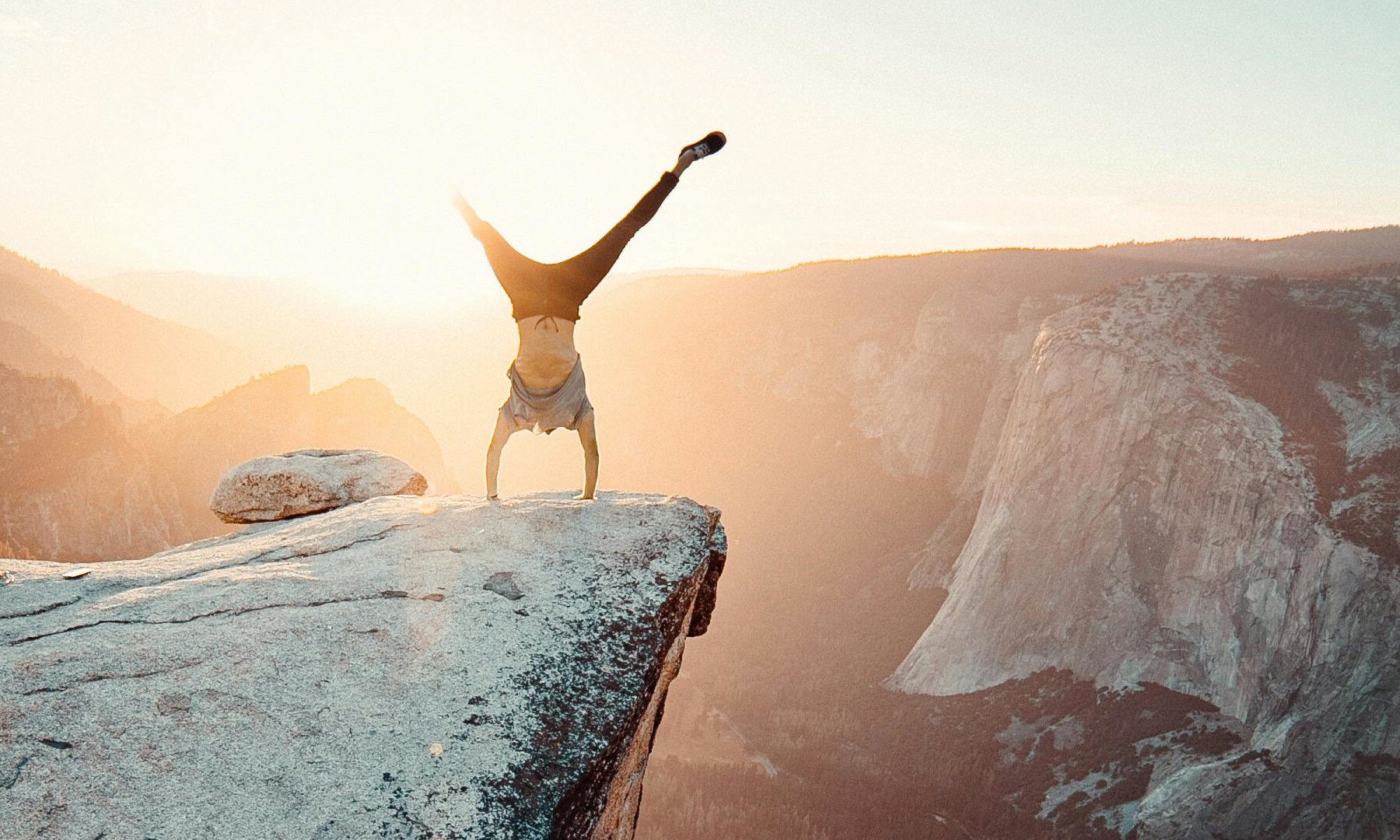 Das Bild zeigt einen Mann im Handstand an einem Felsvorsprung.